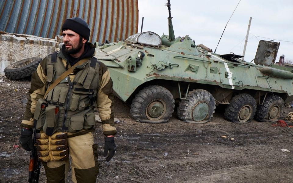 A pro-Russian fighter from Chechnya stands near a damaged Ukrainian armoured vehicle  - Getty