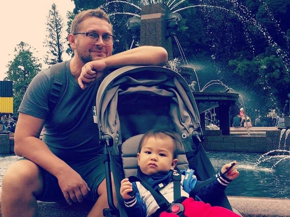 Man sitting with a baby in front of a fountain.