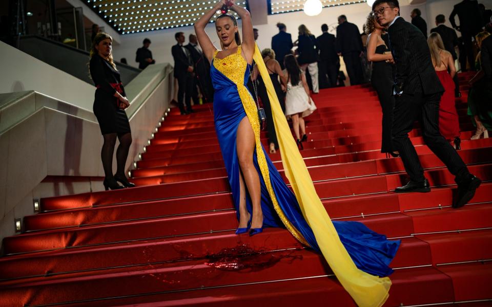 A person wearing a dress in colours of the Ukrainian flag pours a red substance over themselves at the premiere of the film 'Acide' at the 76th international film festival in Cannes, France - Daniel Cole/AP