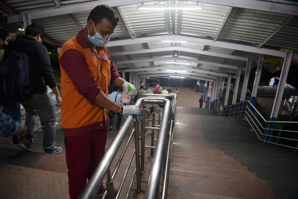 A worker wearing a facemask amid concerns over the spread of the COVID-19 disinfects the hand rail of a staircase at New Jalpaiguri railway station on the outskirts of Siliguri.