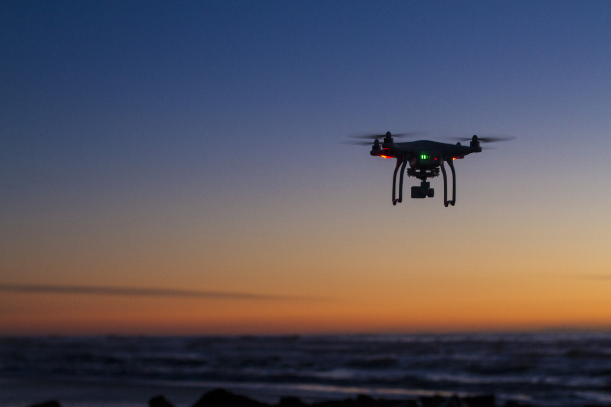 Drone in air over ocean at dawn, drone on right in focus, ocean and horizon blurred in the background