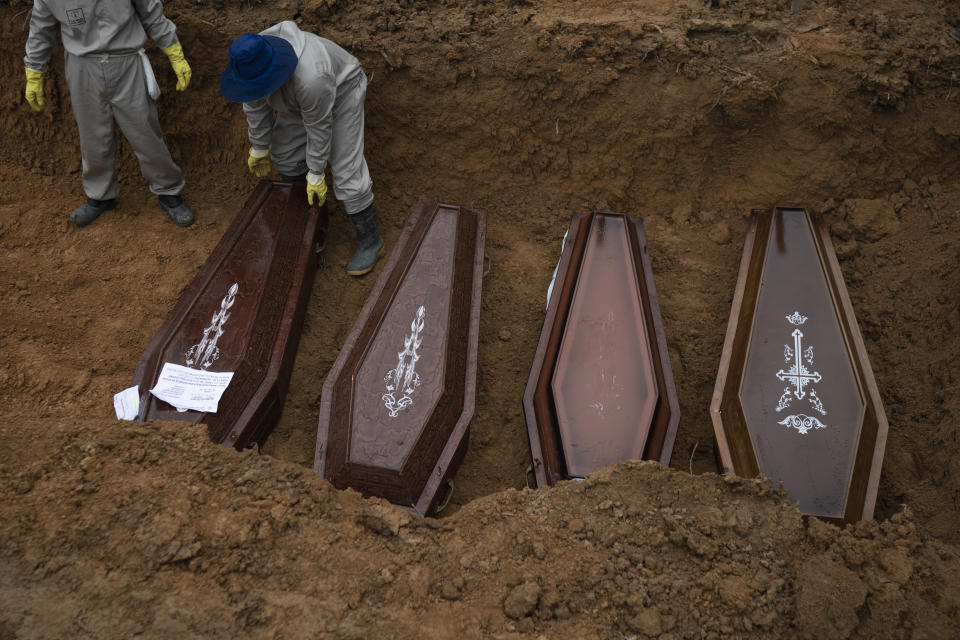 Cemetery workers place coffins in a common grave during a funeral at the Nossa Senhora Aparecida cemetery, amid the new coronavirus pandemic in Manaus, Brazil, Wednesday, May 13, 2020. The new section of the cemetery was opened last month to cope with a surge in deaths. (AP Photo/Felipe Dana)