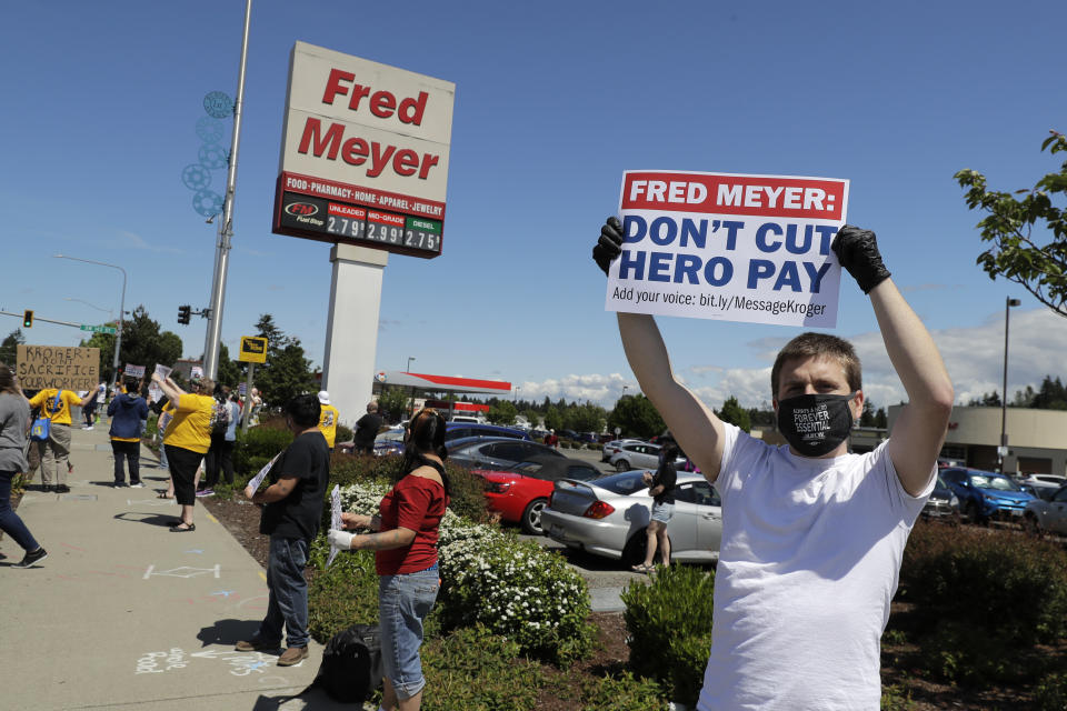 Sherman Jenne, right, a cashier at the Fred Meyer grocery store in Burien, Wash., takes part in a protest outside the store against Fred Meyer's parent company Kroger, Friday, May 15, 2020, that was organized by the United Food and Commercial Workers International Union. Kroger officials have said they are ending the additional $2 hourly "hero pay" bonus that had been paid to workers since late March during the coronavirus pandemic. The company said Friday it will now offer one-time bonus payments of $400 and $200 for full- and part-time employees to be paid in two installments. (AP Photo/Ted S. Warren)