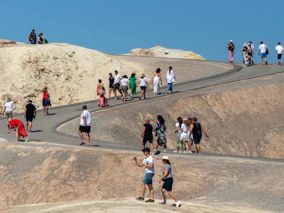 A sloping road down the side of a sand dune where a large group of people are walking together.