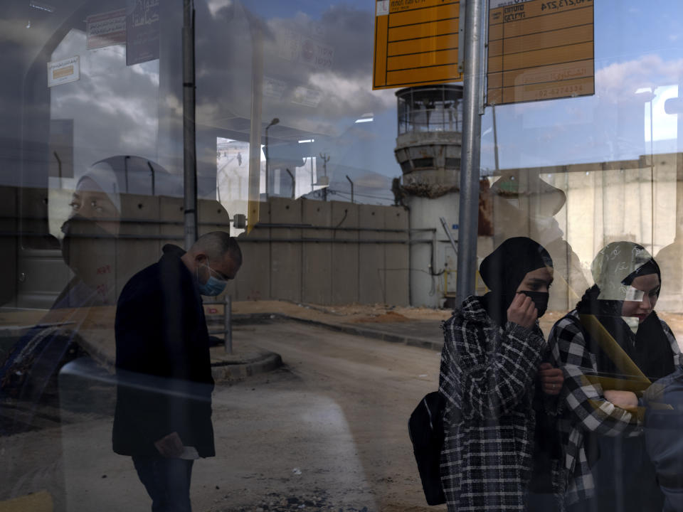 Palestinian passengers get on a bus next to a section of Israel's separation barrier after crossing into Israel through Qalandia checkpoint between the West Bank city of Ramallah and Jerusalem, Monday, Jan. 31, 2022. Twenty years after Israel decided to built its controversial separation barrier amid a wave of Palestinian attacks, it remains in place, even as Israel encourages its own citizens to settle on both sides and admits tens of thousands of Palestinian laborers. (AP Photo/Oded Balilty)