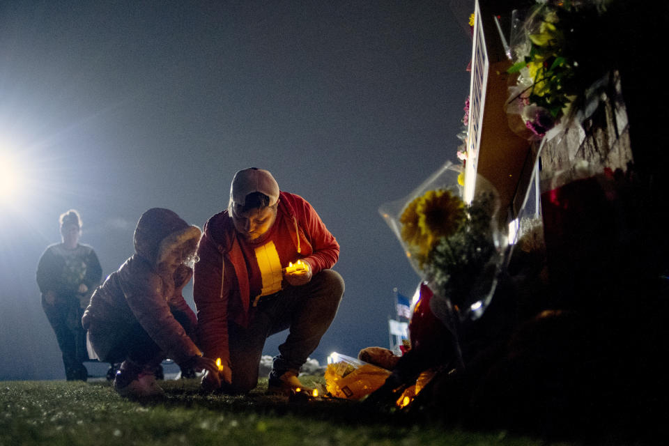 Waterford resident Andrew Baldwin, cousin of Madisyn Baldwin, places candles at the base of a a memorial with his 5-year-old daughter Ariyah Baldwin on Wednesday, Dec. 1, 2021 outside of Oxford High School in Oxford, Mich. Madisyn Baldwin, 17, was one of four teens killed in Tuesday's school shooting. A 15-year-old sophomore opened fire at his Michigan high school on Tuesday, killing four students, including a 16-year-old boy who died in a deputy’s patrol car on the way to a hospital, authorities said. (Jake May/The Flint Journal via AP)