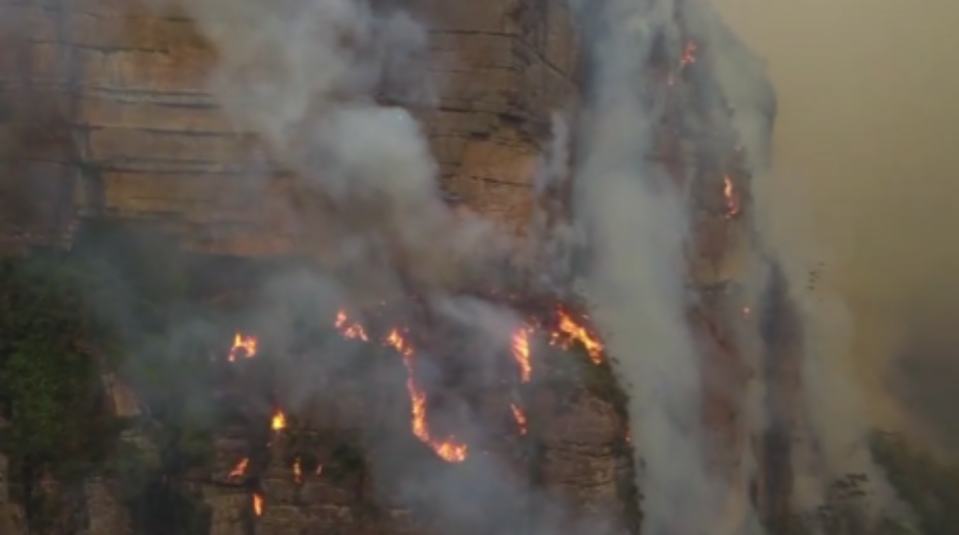 Fire can be seen tumbling down the side of a mountain as bushfires continue to sweep across Australia. (Caters)