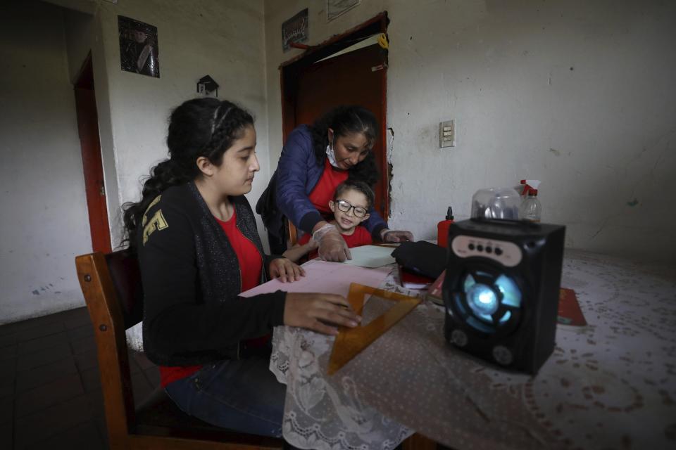 Fanny Mendez, right, mother of 14-year-old Marlene Beltran, left, and Felipe Beltrán, 5, helps her children at home to make a cube out of paper as they listen to an hour-long lesson broadcast by the Bacata Stereo radio station during the lockdown to prevent the spread of the new coronavirus in Funza, Colombia, Wednesday, May 13, 2020. The Beltrans work on dairy farms and have no internet connection at home, so the hour-long radio lesson developed by the municipal government keeps the children busy while schools are closed. (AP Photo/Fernando Vergara)