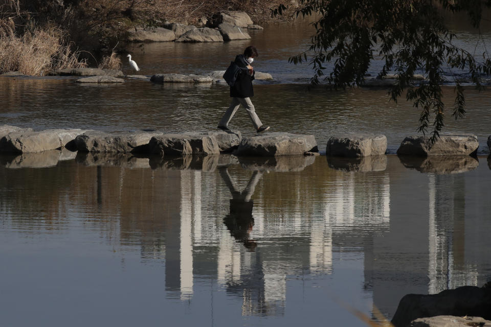 A woman wearing a face mask as a precaution against the coronavirus, crosses a stream at Cheonggye stream in Seoul, South Korea, Thursday, Nov. 26, 2020. (AP Photo/Lee Jin-man)