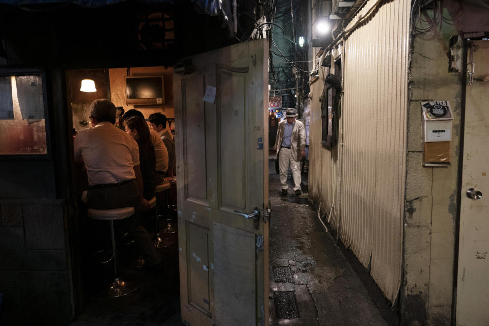 A man, right, makes his way through a narrow passageway between two buildings at the Golden Gai in the Shinjuku district of Tokyo, July 17, 2019. (AP Photo/Jae C. Hong)