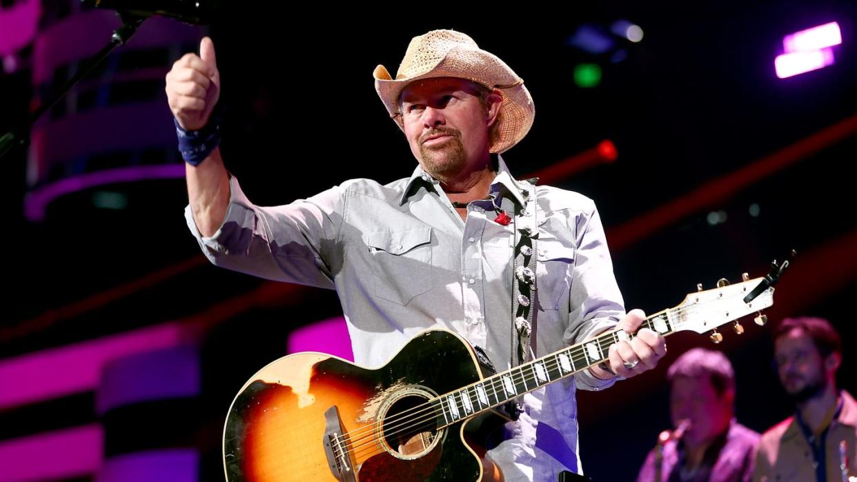 toby keith giving a thumbs up gesture as he holds a guitar while performing at a concert