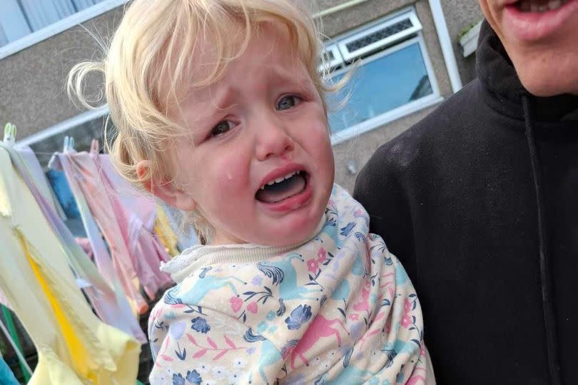 A young girl crying. She is holding out her hand which appears to be bleeding