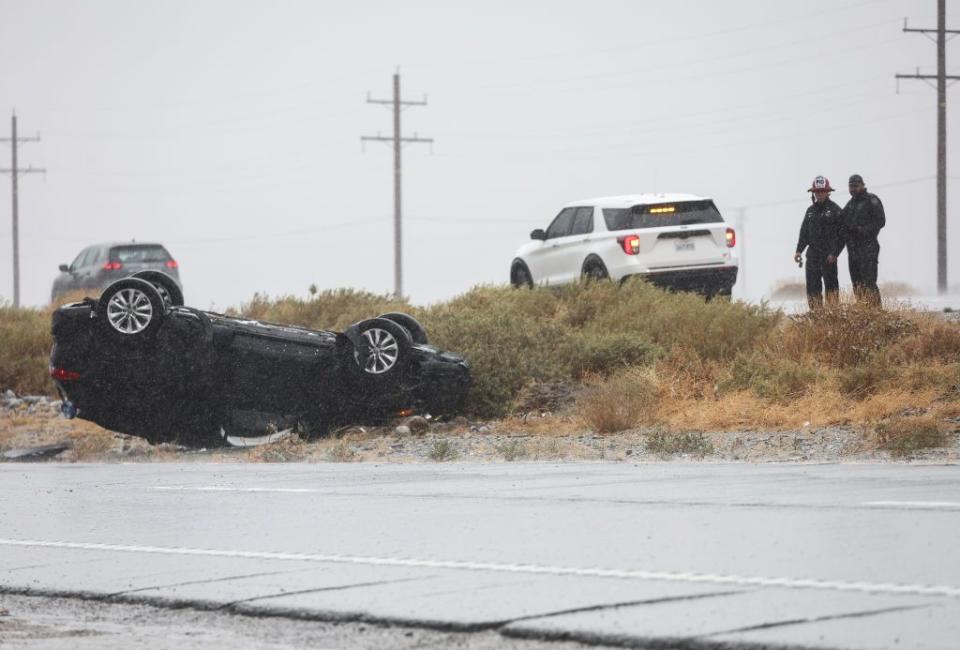 First responders keep watch near a vehicle that flipped over during rainfall from approaching Tropical Storm Hilary near Palm Springs, California.