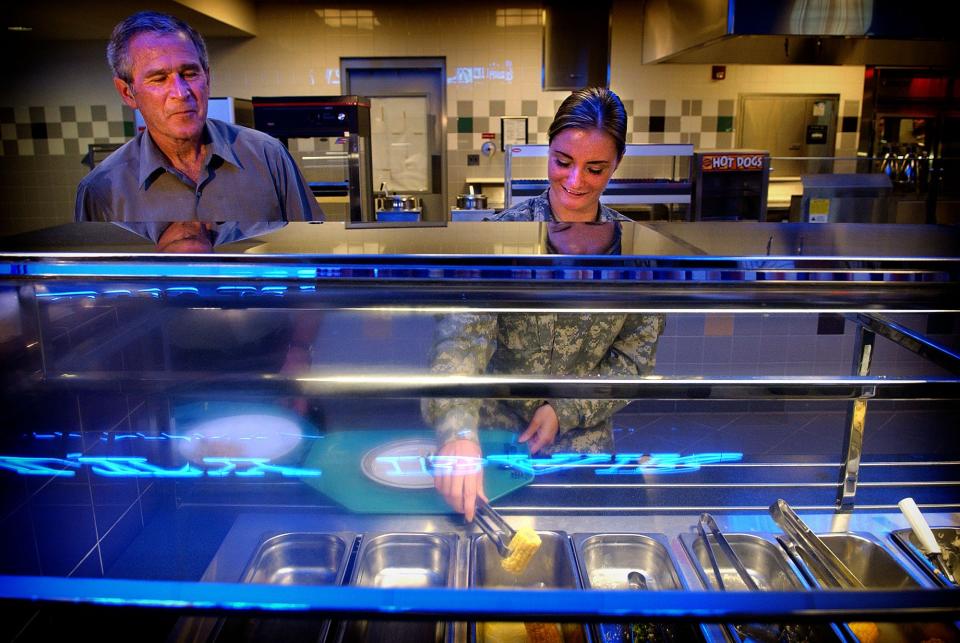 President George W. Bush looks over at Pfc. Samantha Pettit, right, as she dishes up her plate at a 82nd Airborne dining facility Tuesday, July 4, 2006.