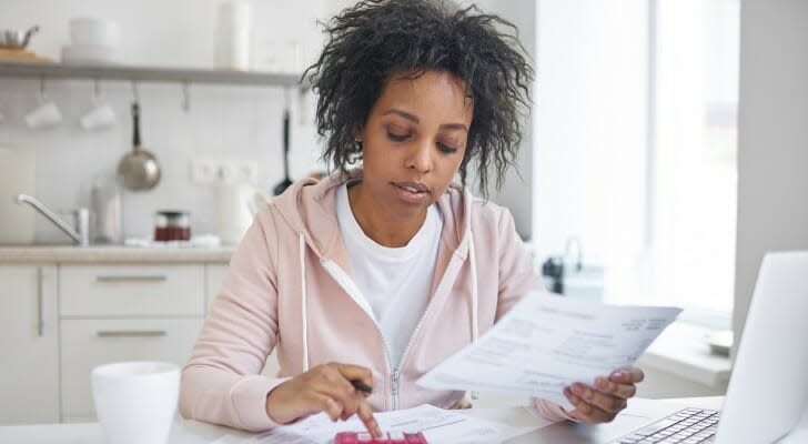 Image shows a woman sitting at a table with a calculator and bills in front of her; she is squaring away her latest financial statements. SmartAsset analyzed various data to identify where Americans are most and least financially literate. 