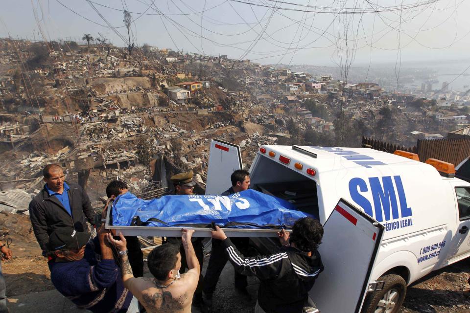 Residents and rescue workers remove a body from the place where a forest fire burned several neighbourhoods in the hills in Valparaiso city