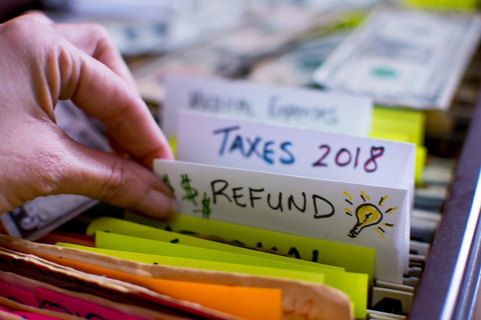 Hand pulling out file in filing cabinet with tax forms and papers with words Refund and Taxes 2018 handwritten on file folder conceptual dollar signs images and light bulb for ideas on tax refund conceptual financial planning photography