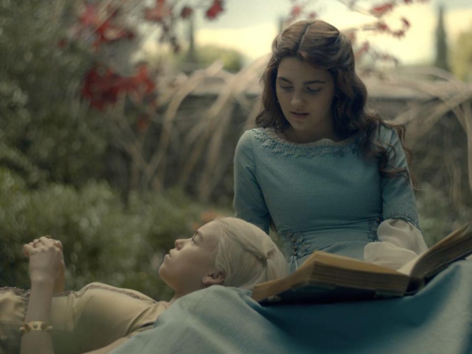 Two girls sitting together on the ground, one with her head in the other's lap.