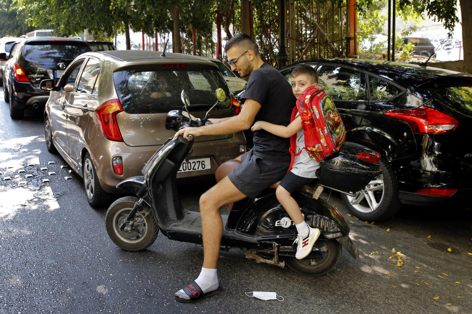 A man picks up his son from school on a scooter, in Beirut, Lebanon, Wednesday, Sept. 29, 2021. This fall, Lebanon's schools have been gripped by the same chaos that has overwhelmed everything else in the country in its historic economic meltdown. The start of the academic year has been postponed repeatedly because thousands of teachers are on strike, demanding adjustments in their salary to cope with hyperinflation. (AP Photo/Bilal Hussein)