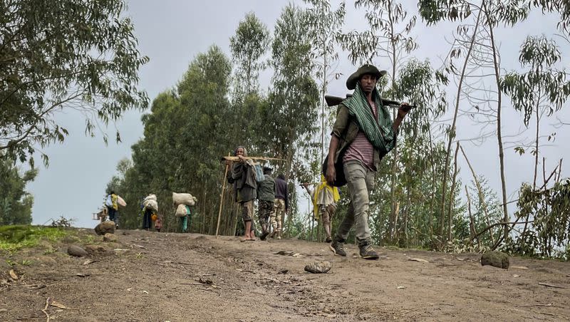 An unidentified armed militia fighter walks down a path as villagers flee with their belongings in the other direction, near the village of Chenna Teklehaymanot, in the Amhara region of northern Ethiopia on Sept. 9, 2021.