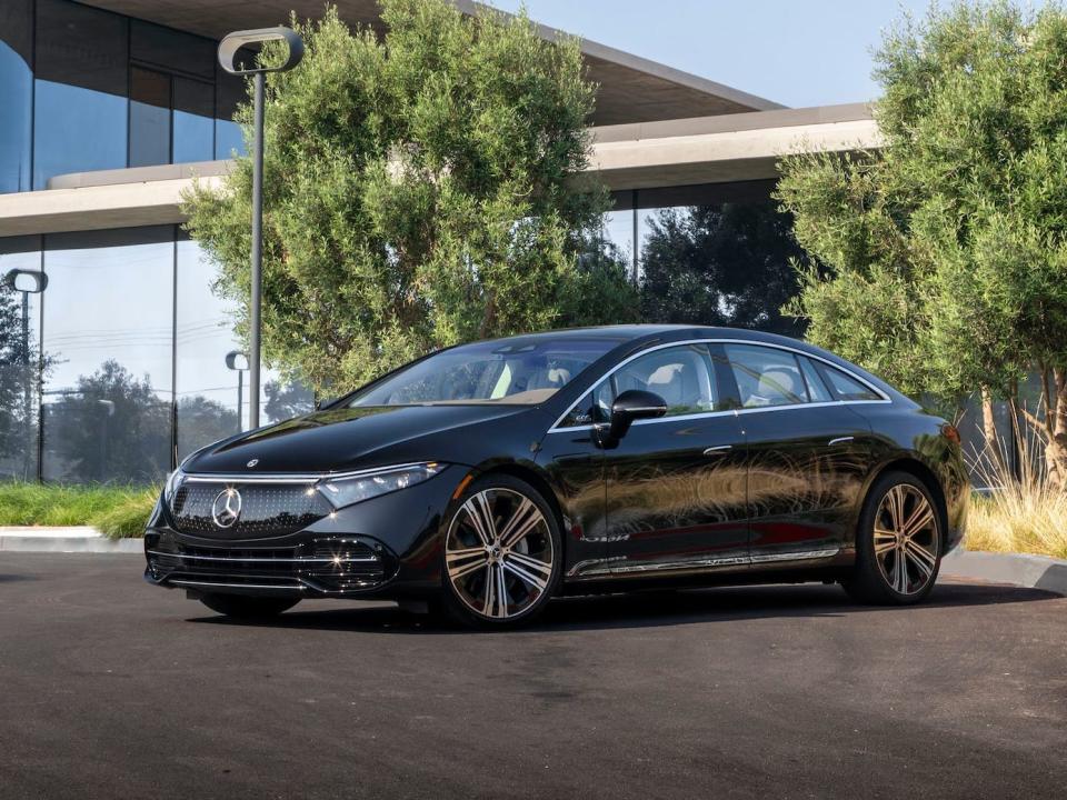 A black Mercedes-Benz EQS 450+ electric car parking in front of a modern glass-enclosed home.