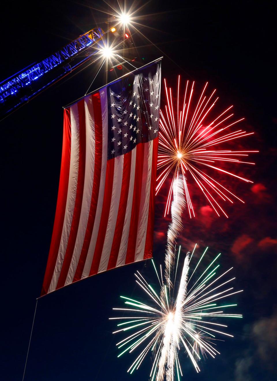 Fireworks fill the sky in 2019 behind a large flag hung from a Freehold Borough firetruck at Freehold Raceway.