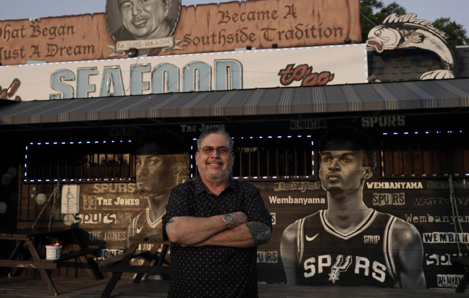 Businessman and San Antonio Spurs fan Roland Ramirez poses with a mural of Victor Wembanyama, a 7-foot-3 French basketball star, that artist Nik Soupe painted on the side of his seafood restaurant in San Antonio, Thursday, June 15, 2023. The San Antonio Spurs are expected to make Wembanyama the No. 1 pick in the NBA draft. (AP Photo/Eric Gay)