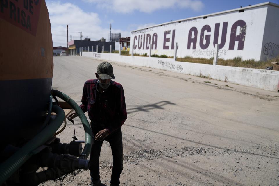 Augustin Rodriguez gets hoses ready on the back of his water truck as he delivers at a home across the street from a large sign that reads "conserve water," in Spanish, Tuesday, May 9, 2023, in Tijuana, Mexico. Among the last cities downstream to receive water from the shrinking Colorado River, Tijuana is staring down a water crisis. (AP Photo/Gregory Bull)