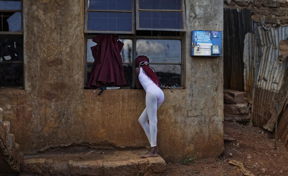 In this photo taken Friday, Dec. 9, 2016, a young ballerina looks through the window at others practicing under the instruction of Kenyan ballet dancer Joel Kioko, 16, in a room at a school in the Kibera slum of Nairobi, Kenya. In a country not usually associated with classical ballet, Kenya's most promising young ballet dancer Joel Kioko has come home for Christmas from his training in the United States, to dance a solo in The Nutcracker and teach holiday classes to aspiring dancers in Kibera, the Kenyan capital's largest slum. (AP Photo/Ben Curtis)