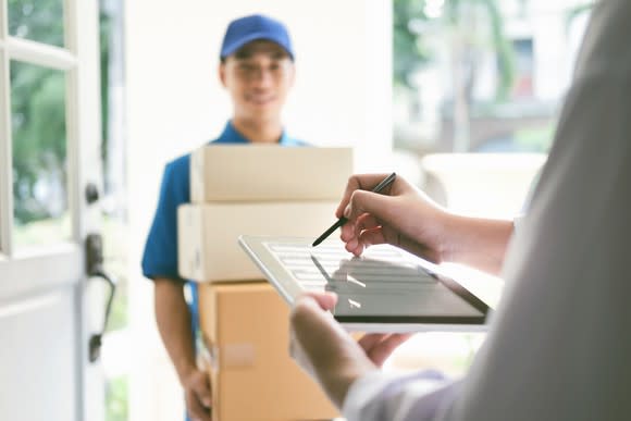 A delivery man holding several boxes while another man signs for them.