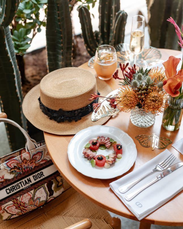 a photo of a cafe table with a plate of food and a dior book tote bag as well as a hat, taken during the dior cafe pop up takeover at sentul pavilion