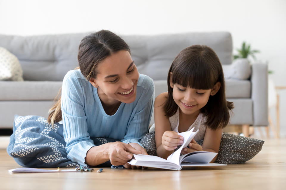 Woman and child lying on floor, smiling while writing in a notebook together