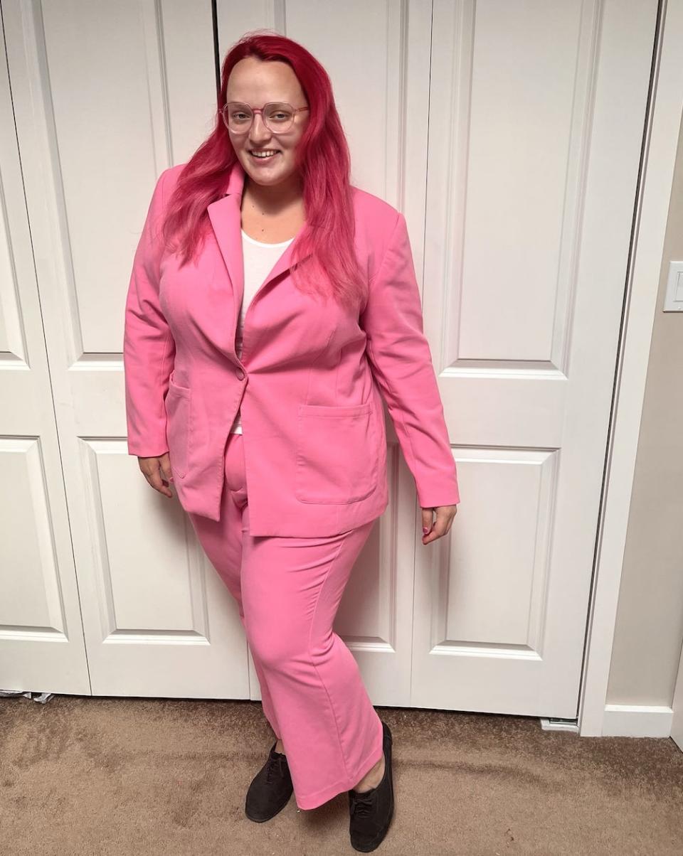 The writer wearing a pink suit with black boots and a white shirt underneath