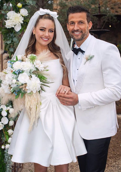 A photo of Tim Robards wearing a white tuxedo jacket and April Rose Pengilly wearing a white wedding dress on set of their wedding on Neighbours.