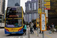 People queue to board a double-decker bus in front of an under-construction residential building, in Hong Kong