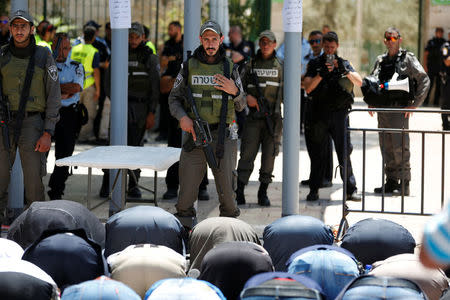 Palestinians pray as Israeli police officers look on by newly installed metal detectors at an entrance to the compound known to Muslims as Noble Sanctuary and to Jews as Temple Mount in Jerusalem's Old City July 16, 2017. REUTERS/Ronen Zvulun