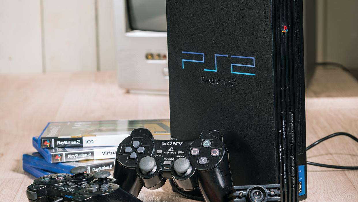  A PS2 games console standing next to some of the best PS2 games and a black controller. . 