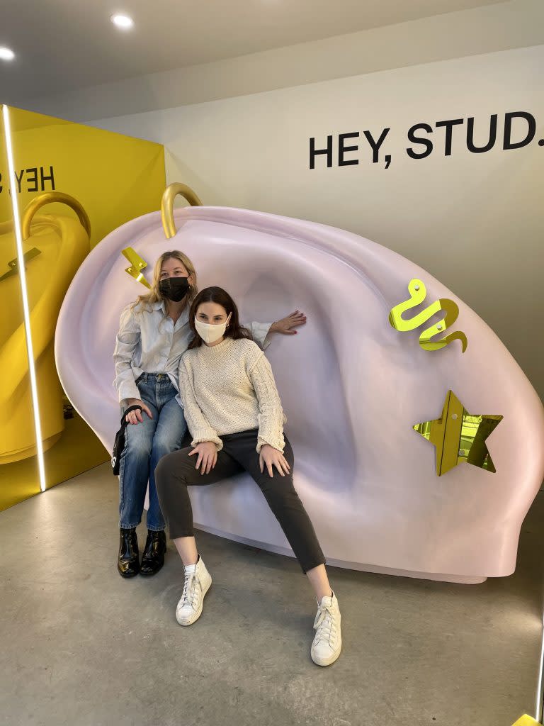 Studs founders Anna Harman and Lisa Bubbers sitting on a giant chair shaped like a pierced ear