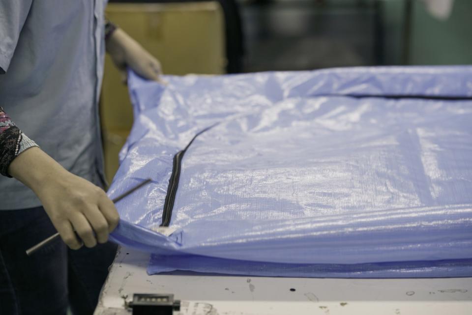 A worker holds the corners of a flat blue bag with black zipper