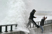 Two women jump off a seawall as they photograph rough surf along Lynn Shore Reservation in the aftermath of a snowstorm, Tuesday, Feb. 2, 2021, in Lynn, Mass. A sprawling, lumbering winter storm has walloped the Eastern U.S., shutting down coronavirus vaccination sites, closing schools and halting transit. (AP Photo/Elise Amendola)