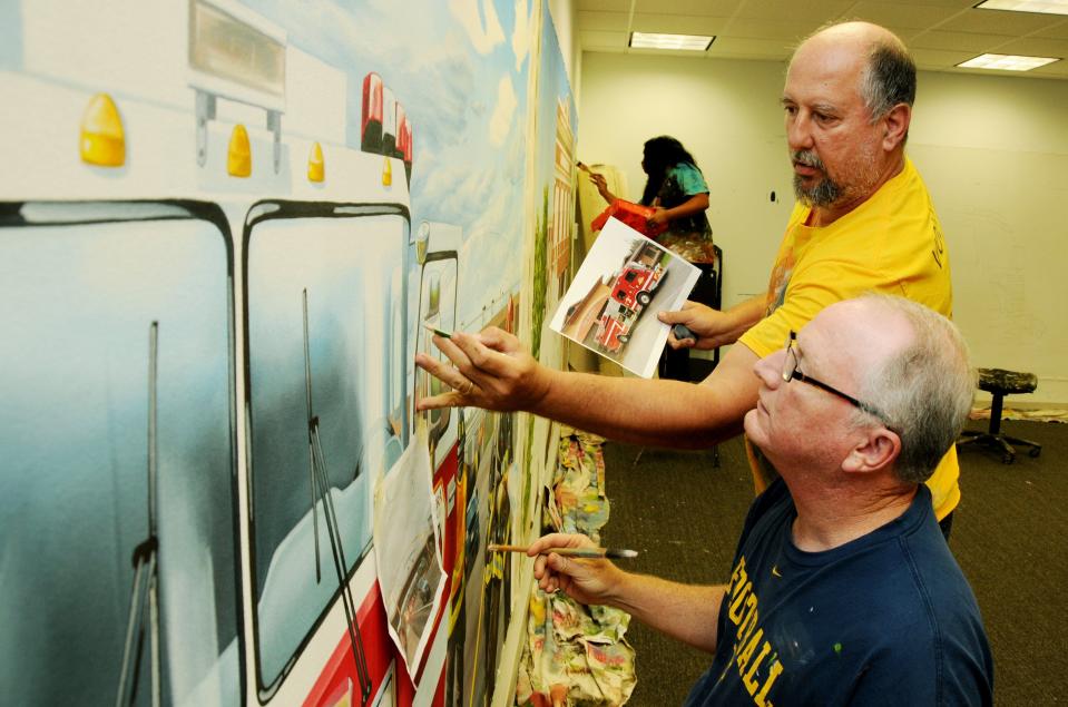 Firehouse Subs muralist Joe Puskas and artist Keith Jones paint details on a mural that will be part of the decor of one of the chain's newest restaurants in October 2017.