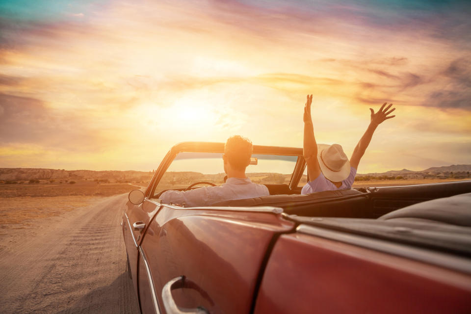 Two people enjoying a ride in a convertible with open arms under a sunset, expressing freedom and joy