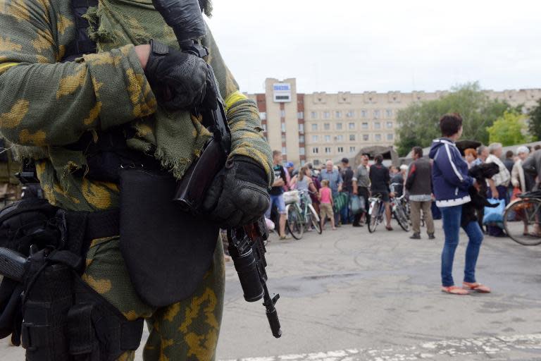 A Ukrainian soldier stands guard as residents wait in line to receive food from employees of the Emergency Ministry near City Hall in the eastern city of Slavyansk, on July 6, 2014