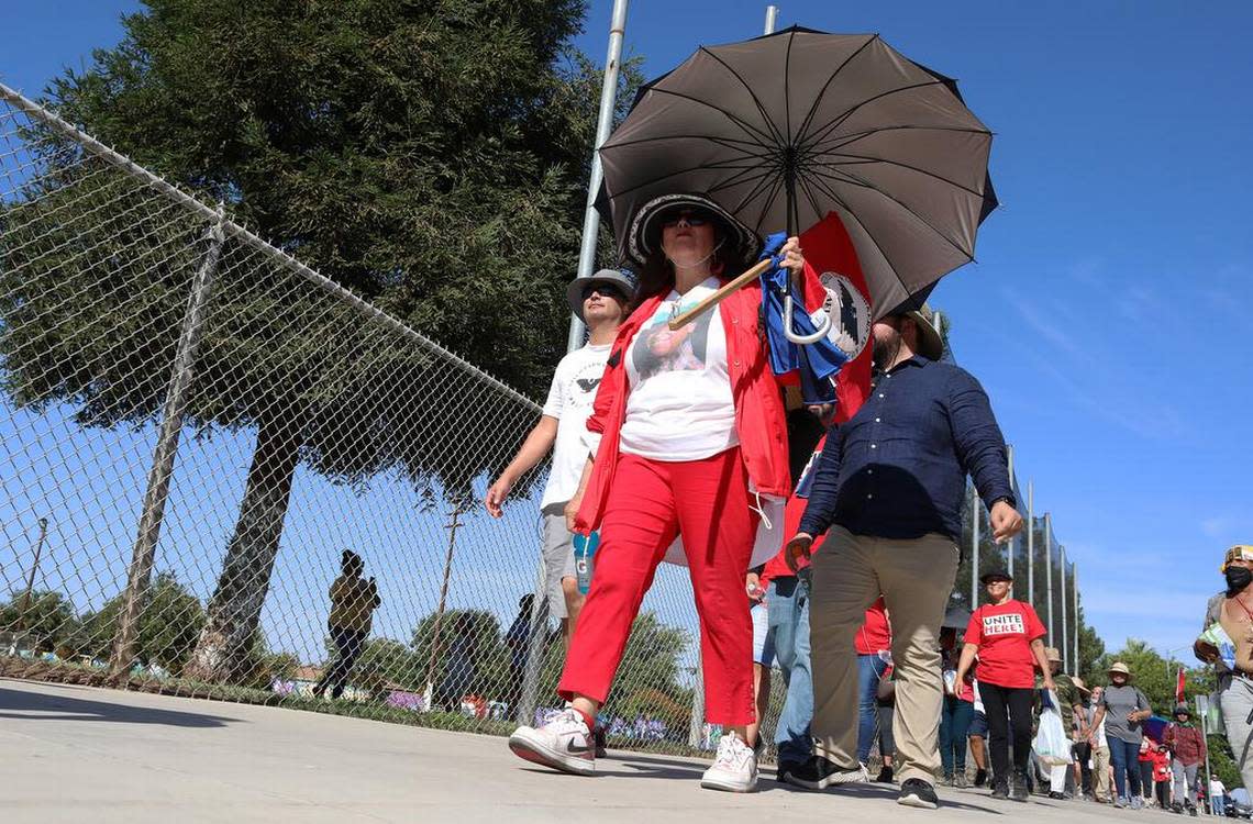 A woman uses an umbrella to protect herself from the sun during the 'March for the Governor's Signature' as it arrived at Calwa Park on Aug. 11, 2022. The 24-day march, which started Aug. 3 in Delano, ended its ninth day.