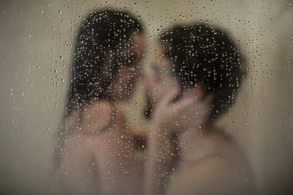 Two unidentified people in an intimate moment behind a fogged glass with water droplets. Faces are close, hands touching