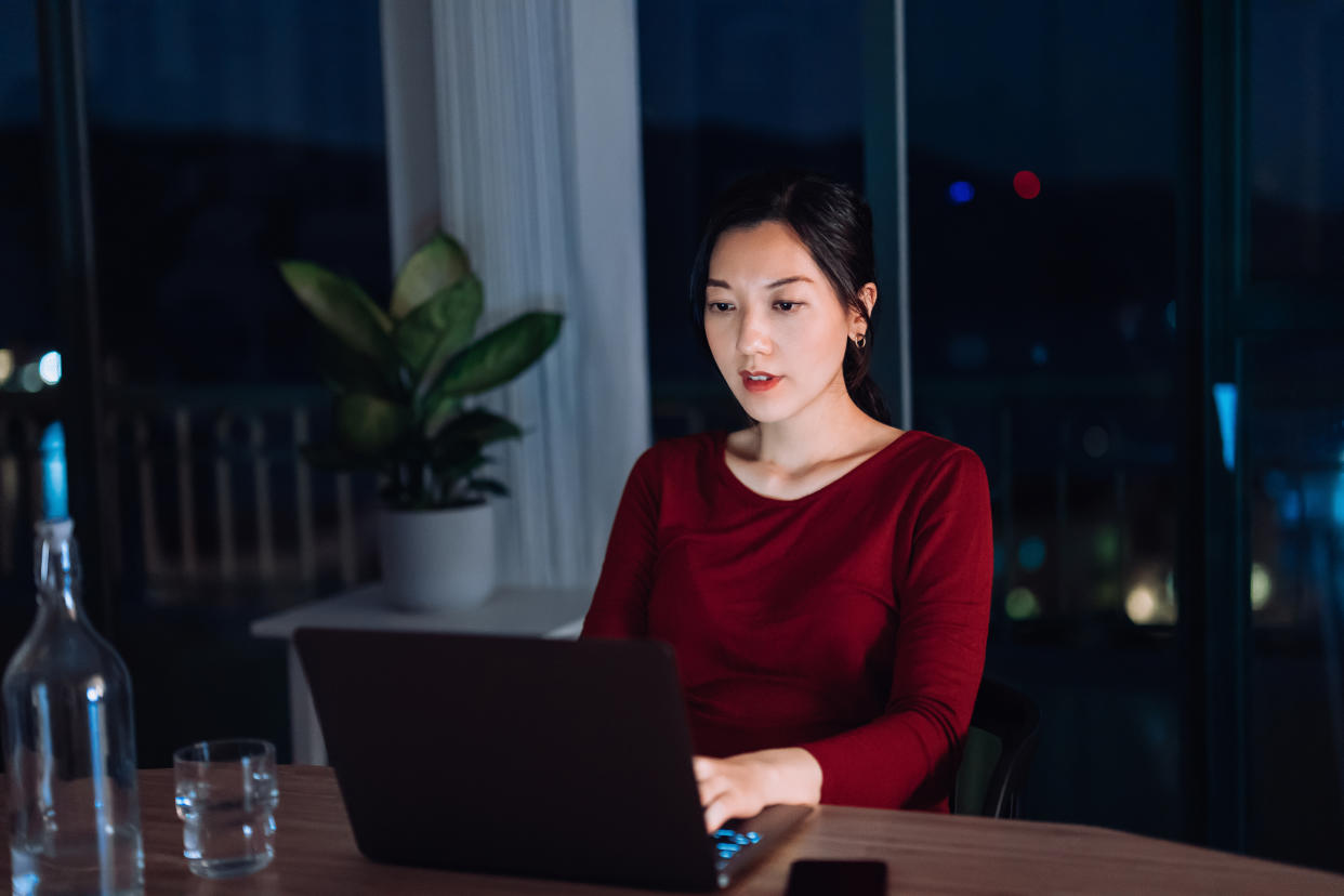 Young Asian businesswoman on video conference with laptop while working from home in the evening. Focused female entrepreneur is sitting on her desk in home office