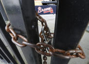 FILE - In this March 31, 2020, file photo, the third base gate to Truist Park, home of baseball's Atlanta Braves, is chained shut in Atlanta. A year after the worldwide coronavirus pandemic stopped all the games in their tracks, the aftershocks are still being felt across every sector. (Curtis Compton/Atlanta Journal-Constitution via AP, File)
