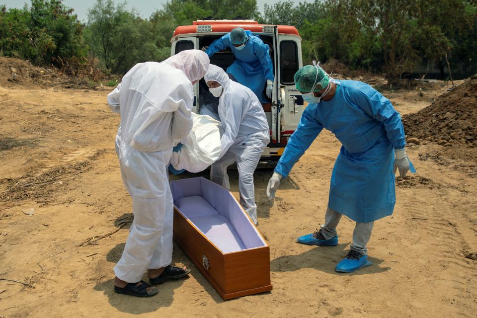 Los trabajadores del cementerio y los familiares bajan de la ambulancia de Mohammad el cuerpo de un fallecido por coronavirus. (Foto: Danish Siddiqui / Reuters).