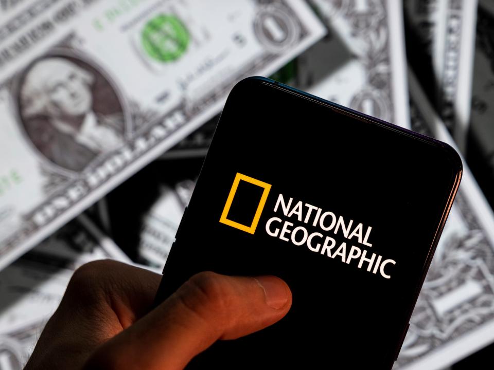 n this photo illustration the American science, culture and nature magazine and digital cable and television network National Geographic (NG) logo seen displayed on a smartphone with USD (United States dollar) currency in the background. (Photo Illustration by Budrul Chukrut/SOPA Images/LightRocket via Getty Images)