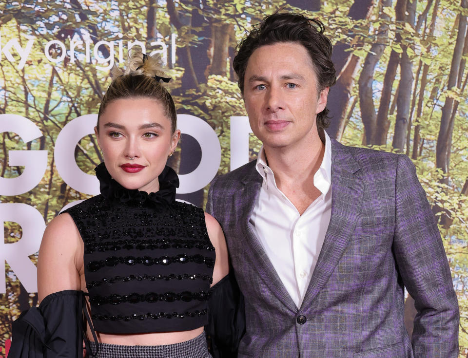 Zach Braff and Florence Pugh posing together on the red carpet, she's wearing a black crop top and high-waisted pants, he's in a purple plaid suit